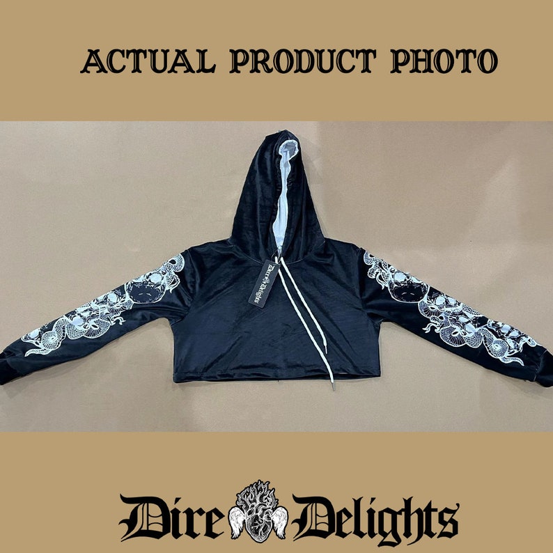 May include: Black cropped hoodie with a white skull and snake design on the sleeves. The hoodie has a drawstring hood and a tag that says "Dire Delights".