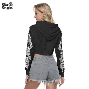 May include: Black cropped hoodie with long sleeves featuring a white snake and skull design. The hoodie has a drawstring hood.