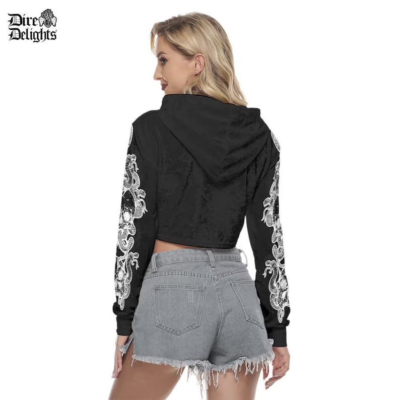 May include: Black cropped hoodie with long sleeves featuring a white snake and skull design. The hoodie has a drawstring hood.