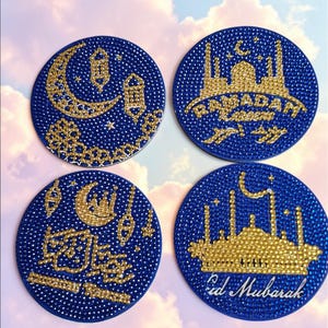 May include: Four round blue coasters with gold and white embellishments. Each coaster features a different design: a crescent moon, a mosque, Arabic calligraphy, and a mosque with the words "Ramadan Kareem" and "Eid Mubarak".