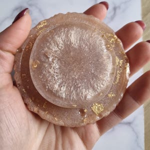 May include: A set of three resin coasters in shades of pink and white, with gold leaf accents. The coasters have a glossy finish and a circular shape, perfect for protecting surfaces from drink rings.