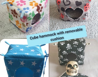 Puede incluir: Cuatro hamacas cúbicas diferentes para mascotas pequeñas. Las hamacas están hechas de tela suave y tienen un cojín extraíble. Las hamacas están disponibles en cuatro tamaños diferentes. El texto "Cube hammock with removable cushion" y "Available in 4 sizes" es visible en la imagen.