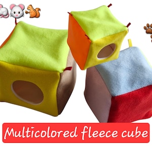 May include: Three brightly coloured fleece cubes for small pets. Each cube features a different colour combination, including green, orange, yellow, blue, and red. The cubes have a circular opening and small red loops at the corners. The text "Multicolored fleece cube" is displayed.