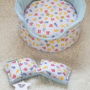 May include: A light blue pet bed with a white and yellow fabric featuring a seahorse, starfish, and seashell pattern. The bed comes with two matching pillows. The tag says "Thank you for your order!"