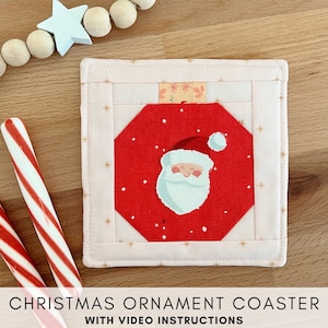 Op de afbeelding: Een roze en rode gestikte onderzetter met een kerstbalontwerp met Sinterklaas. De onderzetter heeft een gouden sterrenpatroon en de tekst "CHRISTMAS ORNAMENT COASTER WITH VIDEO INSTRUCTIONS".