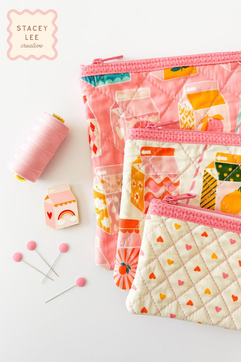 May include: A collection of pink quilted pouches with zipper closures, featuring milk carton and heart patterns. A spool of pink thread, a milk carton pin, and pink-headed pins are also present. The Stacey Lee Creative logo is in the upper left corner.