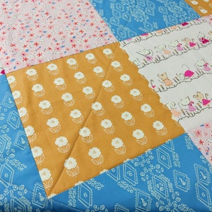 May include: A patchwork quilt with a variety of patterns, including floral, geometric, and a pattern of mice. The quilt is made with a mix of pink, blue, white, and yellow fabrics.
