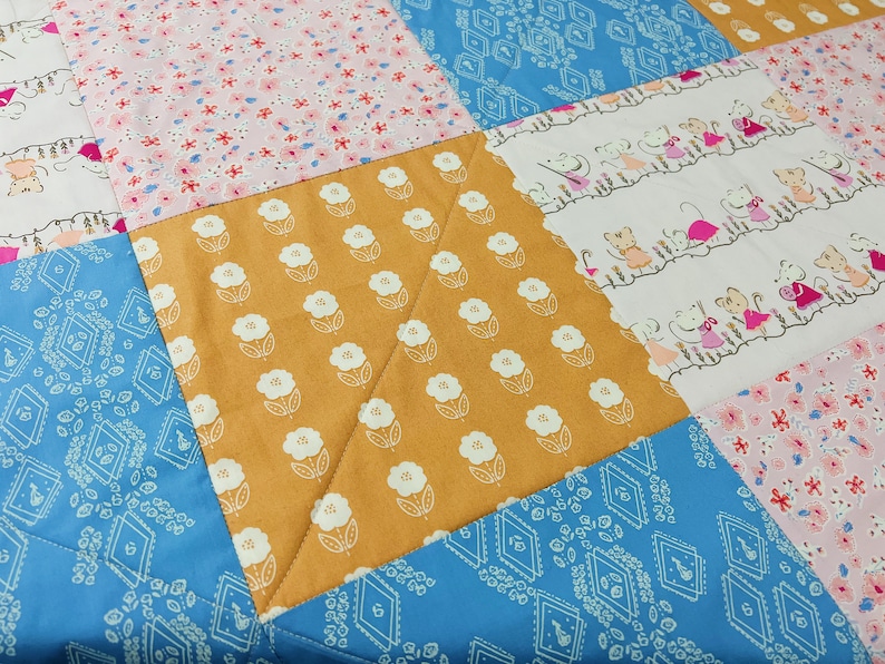 May include: A patchwork quilt with a variety of patterns, including floral, geometric, and a pattern of mice. The quilt is made with a mix of pink, blue, white, and yellow fabrics.