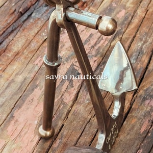 May include: A bronze nautical anchor with the inscription "Our 21st 4/12/24". The anchor, made of metal, features a ring and a pivoting arm. It is displayed on a wooden surface. The design is detailed and maritime-themed.
