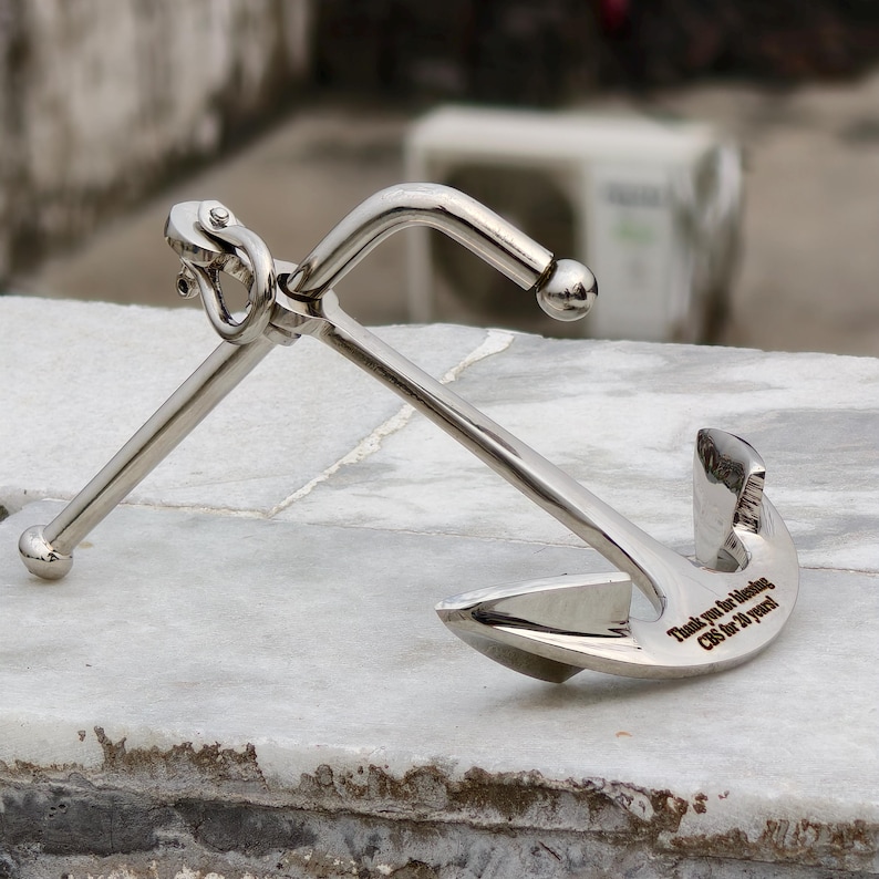May include: A polished silver anchor with a curved shank and two flukes. The anchor has a ring at the top and a crossbar. The text "Thank you for blending CBS for 20 years!" is engraved on the fluke.