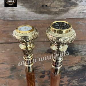 Puede incluir: Dos bastones de paseo decorativos con tapas ornamentadas de color dorado. Una tapa presenta una brújula con una cara negra y marcas doradas. La otra tapa presenta un reloj con una cara blanca y manecillas negras. Ambos bastones tienen ejes de madera marrón.