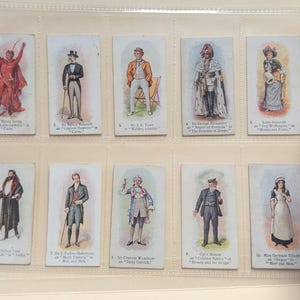 May include: A collection of ten vintage cards featuring illustrations of actors in various theatrical roles. Each card has a number, the actor's name, the role they are playing, and the name of the play. The cards are in a white album with a decorative border.