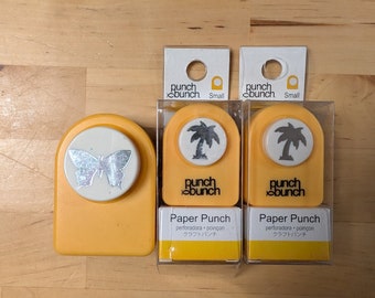 May include: Three yellow paper punch tools with different designs. The first punch is a butterfly, the second is a palm tree, and the third is also a palm tree. Each punch has the words "punch bunch" and "paper punch" printed on it.