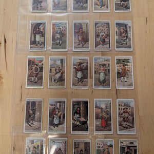 May include: A collection of 25 vintage trading cards featuring illustrations of people in various occupations. The cards are arranged in a clear plastic sheet protector. Each card has a white border and a colorful illustration of a person in a historical setting.