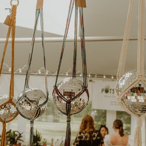 May include: Three macrame plant hangers with silver disco ball ornaments. The hangers are made with different colored cords and have tassels at the bottom.