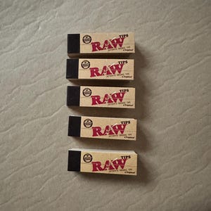 May include: Five packs of RAW rolling tips. Each pack is brown with a red RAW logo and the text "TIPS" and "AUTHENTIC ORIGINAL TIPS" in white. The text "Original" is in red.