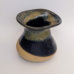 May include: A small, hand-thrown ceramic vase with a wide, flared opening. The vase is glazed in a dark blue and brown color with a light brown band around the bottom.