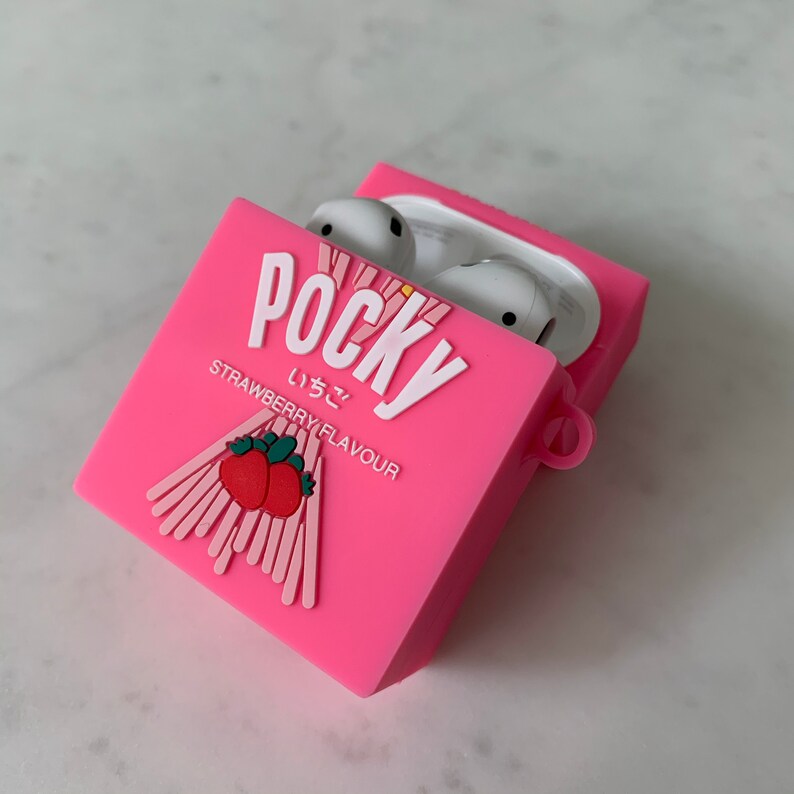 May include: A pink silicone AirPods case with the word "POCKY" in white, along with Japanese text and "STRAWBERRY FLAVOUR". The case features a strawberry and biscuit design. White AirPods are visible inside the open case.