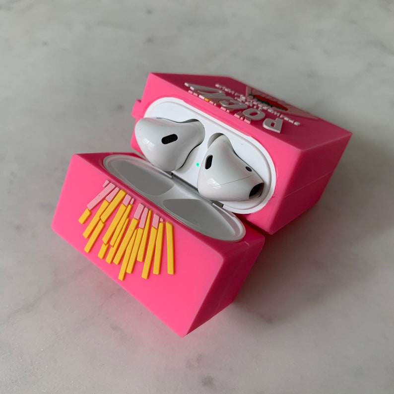 May include: A pink silicone AirPods case shaped like a box of Pocky, with yellow and pink accents. The case is open, revealing white AirPods inside. The word "Pocky" is visible on the case.