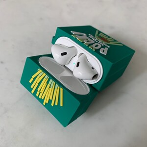 May include: A teal AirPods case shaped like a french fry box, with yellow fries on the front and the word "POG" on the top. The case is open, revealing white AirPods inside.