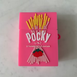 May include: A pink case featuring a Pocky strawberry flavor design. The case has a rectangular shape with a hinged lid. The design includes the word "Pocky" in white, Japanese characters, and a strawberry graphic.