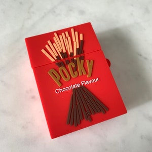 May include: A red case with a Pocky Chocolate Flavour design. The case features a 3D design of Pocky sticks in light brown and dark brown, with the word "Pocky" in brown letters.