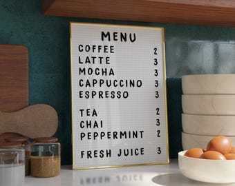 以下が含まれることがあります： 金色の枠のある白いメニューボードに、コーヒーと紅茶の飲み物とその価格がリストされています。 メニューボードは、白いカウンターの上に置かれ、白いボウルが積み重ねられ、卵の入ったボウルが置かれています。