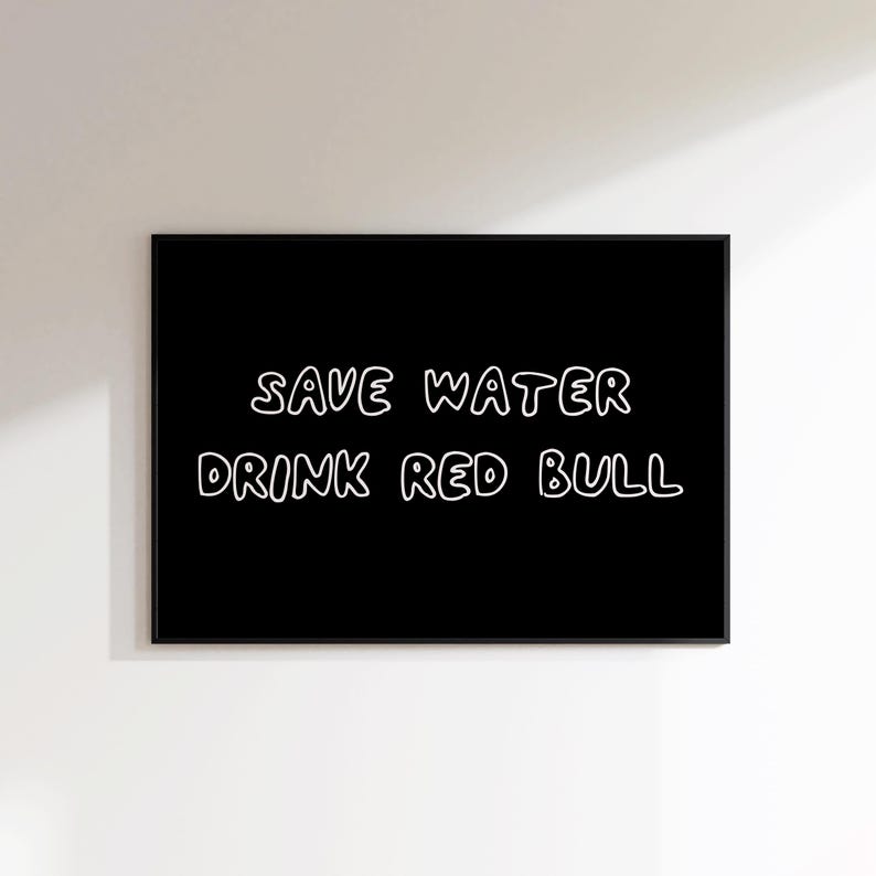 May include: A framed black print with white text that reads "SAVE WATER DRINK RED BULL". The text is in a handwritten style. The print is displayed on a white wall.