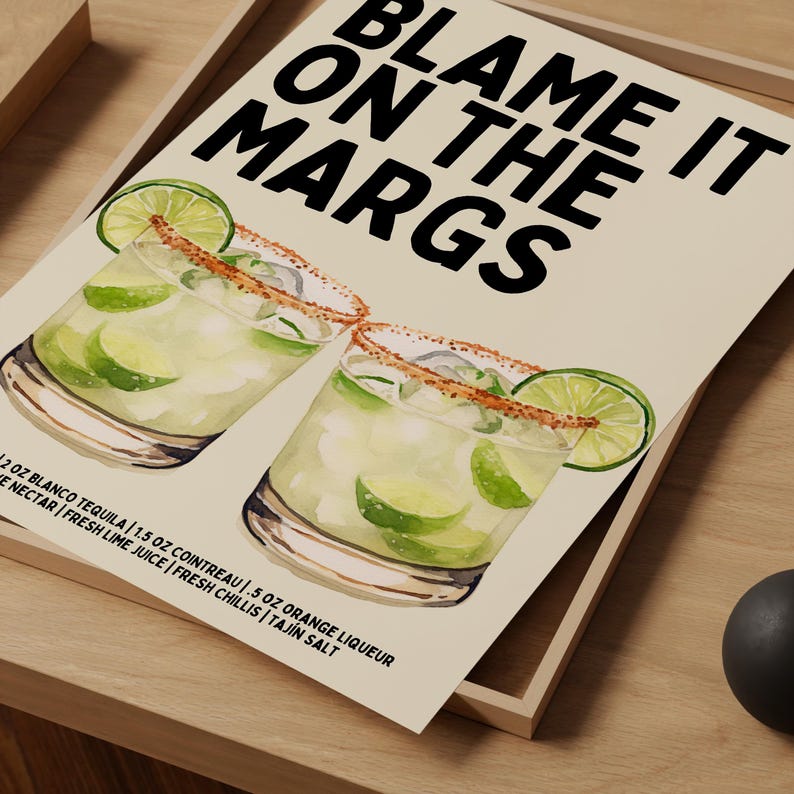 May include: A print featuring two margarita cocktails with lime wedges and a Tajin salt rim. The text "BLAME IT ON THE MARGS" is displayed in bold black letters. The ingredients are listed below the cocktails.