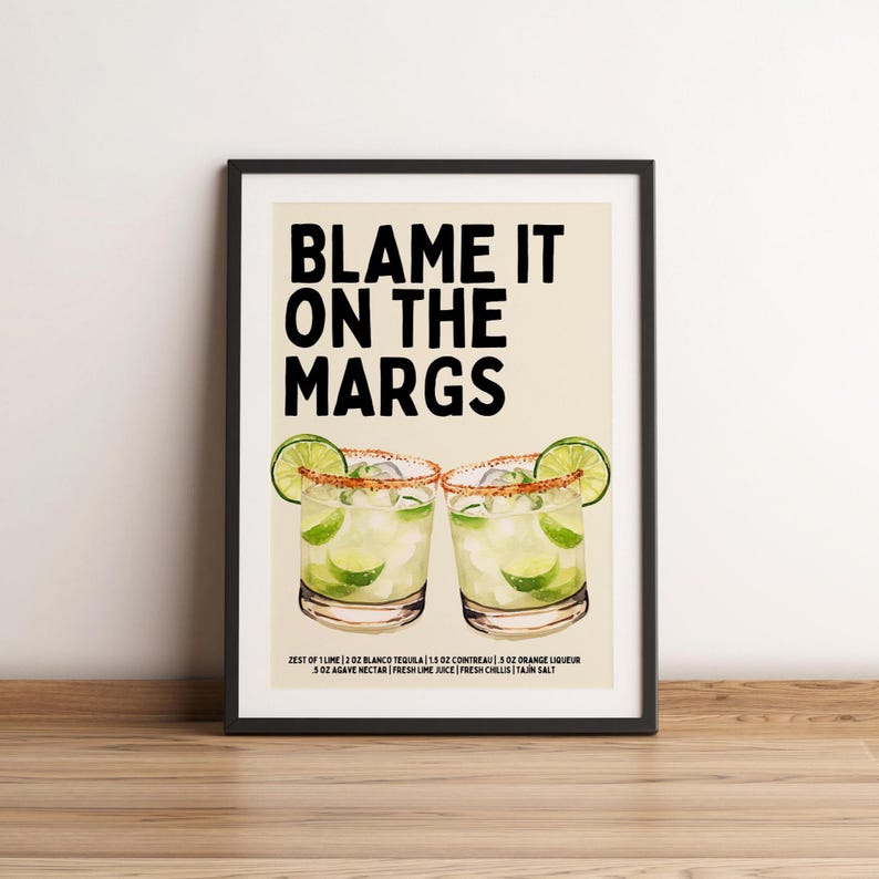 May include: A framed print with the text "BLAME IT ON THE MARGS" above two margarita cocktails. The cocktails are garnished with lime wedges and salt rims. The ingredients are listed below the cocktails.