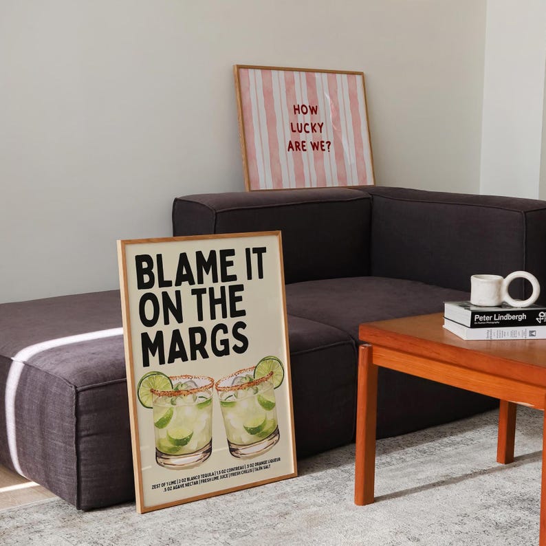 May include: Two framed art prints. One says "Blame it on the Margs" with margarita illustrations. The other says "How lucky are we?" with pink and white stripes. Both are in wooden frames.