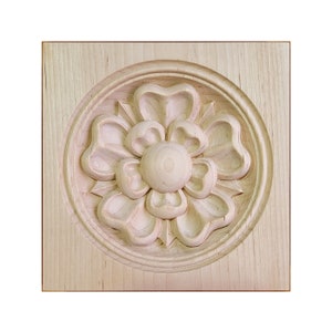 May include: A wooden plaque with a carved floral design. The flower is in a circular frame and has five petals. The plaque is made of light wood and has a natural finish.