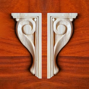 May include: Two wooden corbels with a decorative scroll design. The corbels are light brown and have a smooth finish.