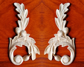 Könnte beinhalten: Zwei verzierte, weiße Holzdekorationen mit einem Blatt- und Eichelmotiv. Die Akzente sind symmetrisch und haben ein geschnitztes, detailliertes Design.