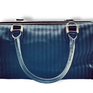 May include: A dark blue handbag with vertical stripes and silver-toned hardware. The bag has two handles and a zipper closure. The handles are attached to the bag with silver metal rings.