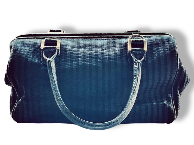 May include: A dark blue handbag with vertical stripes and silver-toned hardware. The bag has two handles and a zipper closure. The handles are attached to the bag with silver metal rings.