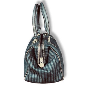 May include: A dark teal handbag with vertical stripes and silver-toned hardware. The bag has two handles and a zipper closure. The zipper pull features a circular logo. The bag's design includes a textured pattern.