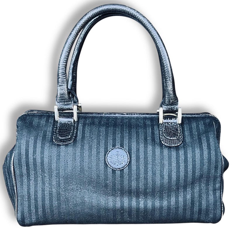 May include: A black handbag with vertical stripes and a rounded shape. The bag has two handles and silver-colored hardware. A small, circular emblem is centered on the front. The bag's design features a textured, patterned surface.