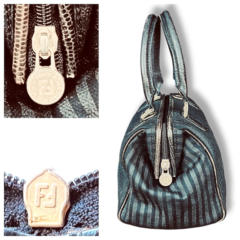 May include: A black and gray striped handbag with silver hardware and two top handles. The bag features a zipper closure with a circular metal pull and the Fendi Roma logo. The bag's design includes a textured pattern.