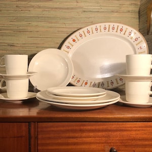 Puede incluir: Un juego de vajilla de cerámica blanca con un patrón geométrico en naranja y dorado. El juego incluye una fuente ovalada grande, dos platos para cenar, dos platos para ensalada, dos tazas y dos platillos.