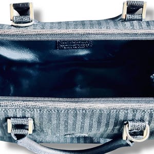 May include: A close-up of a black and gray handbag with a striped pattern. The bag has silver-colored hardware, including handles and clasps. The interior is a dark, glossy material. The bag is open, revealing the inside.