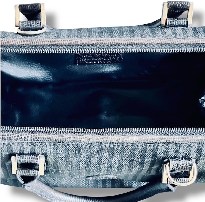 May include: A close-up of a black and gray handbag with a striped pattern. The bag has silver-colored hardware, including handles and clasps. The interior is a dark, glossy material. The bag is open, revealing the inside.