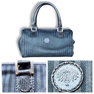 May include: Black handbag with vertical stripe pattern, featuring two handles and silver-tone hardware. The bag has a circular emblem on the front and a zipper closure. The bag is a classic style.