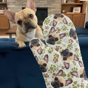 Könnte beinhalten: Ein beiger und weißer Ofenhandschuh mit einem sich wiederholenden Muster aus französischen Bulldoggen-Gesichtern und Pfotenabdrücken. Im Hintergrund ist eine echte französische Bulldogge zu sehen. Der Handschuh ist gesteppt und hat eine Aufhängeschlaufe.