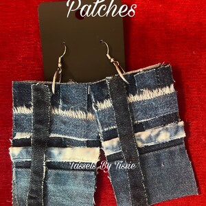 May include: A pair of denim earrings with a patchwork design. The earrings are blue and have a frayed edge. The earrings are labeled "Patches" and "Tassels By Tisse".