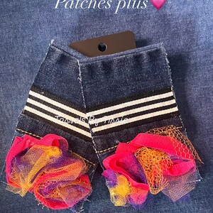 May include: Two denim patches with white stripes and a pink, orange, and purple tulle flower embellishment. The patches are labeled "Tassels By Trissie".
