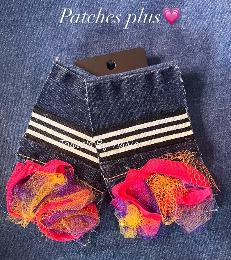 May include: Two denim patches with white stripes and a pink, orange, and purple tulle flower embellishment. The patches are labeled "Tassels By Trissie".