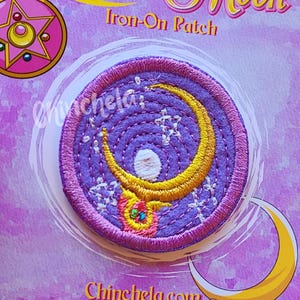 May include: A circular embroidered iron-on patch featuring a yellow crescent moon and a small white pearl on a purple background. The patch is mounted on a purple backing card with the text Sailor Moon Iron-On Patch and Chinchela.com.