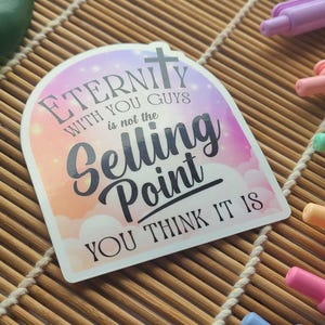 May include: A sticker with the text "Eternity with you guys is not the Selling Point YOU THINK IT IS" in a colorful design. Pastel pens in various colors are scattered around the sticker on a bamboo mat.
