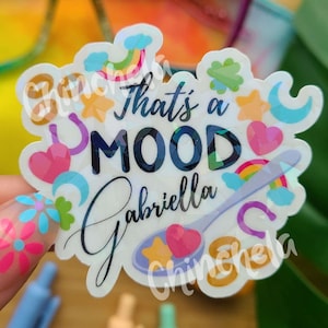 May include: A clear sticker with a rainbow, stars, hearts, and clouds design. The sticker says "That's a MOOD Gabriella Chinchella".